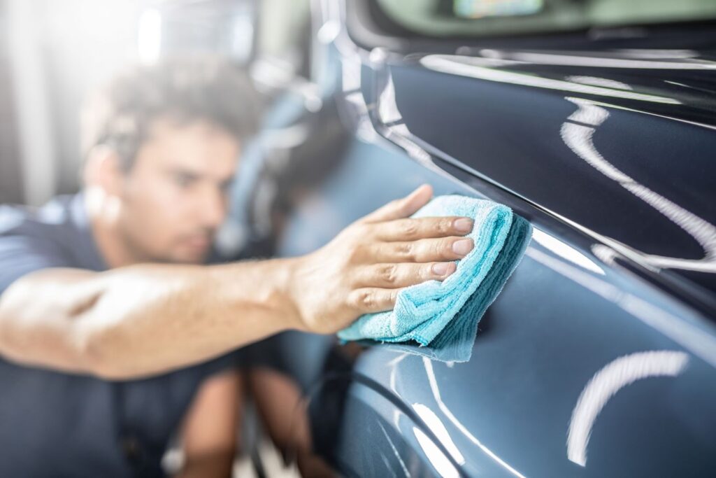 a man preps a blue car's surface for clay bar application by cleaning with a microfiber cloth