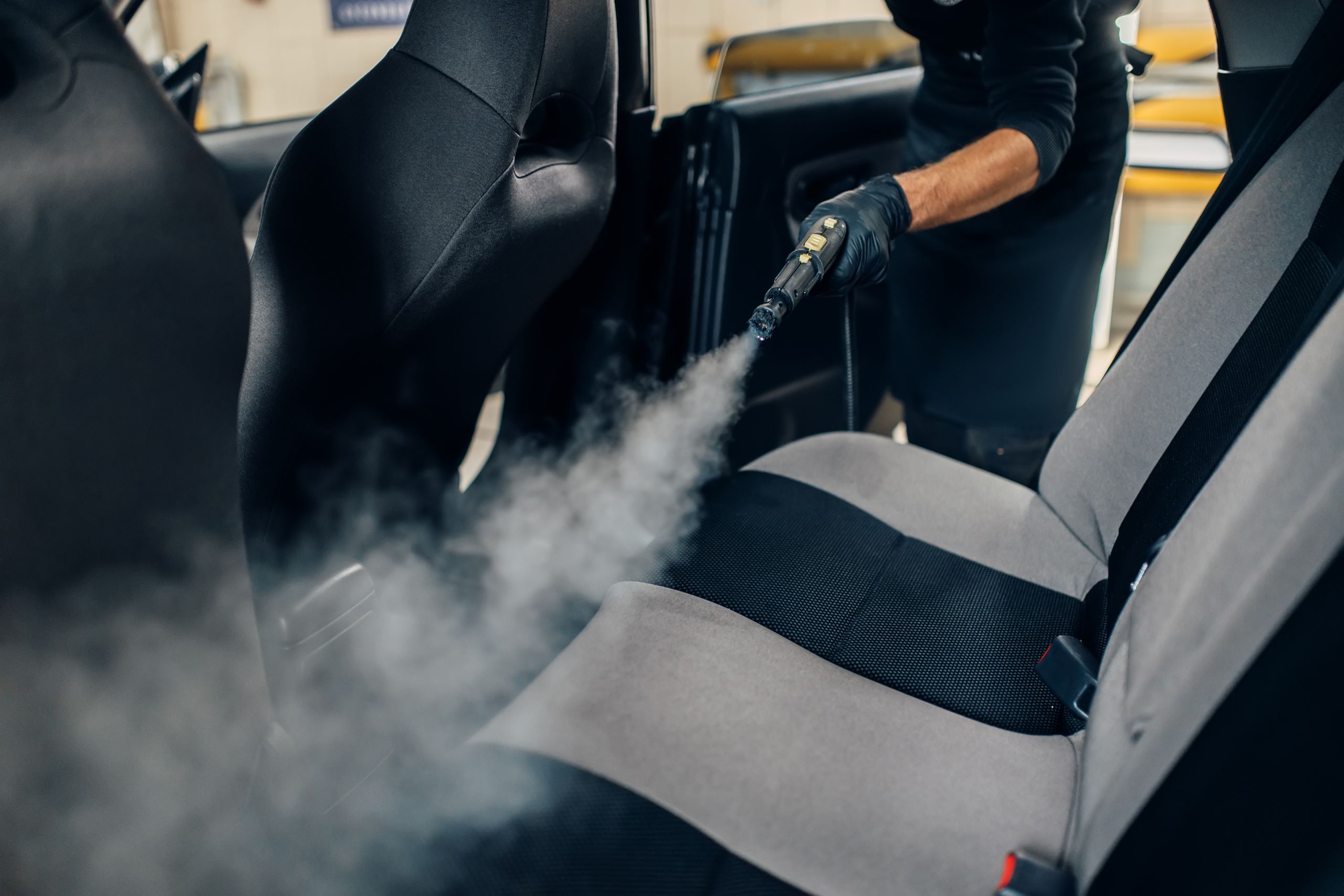 a person spraying steam on the seat of a car to clean it